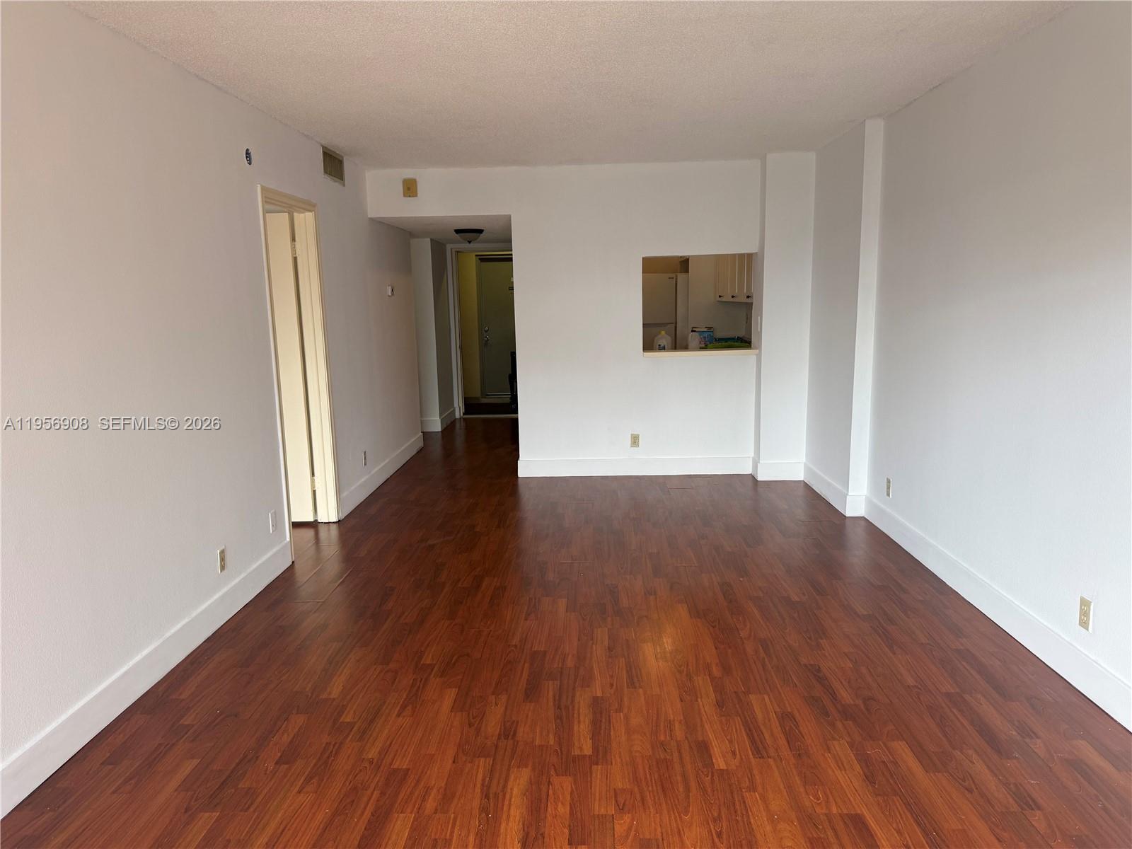 An empty living area features dark wood-look flooring, white walls, and a kitchen pass-through window — 7900 Camino Cir # 403, Miami FL 33143, MIAMI, FL