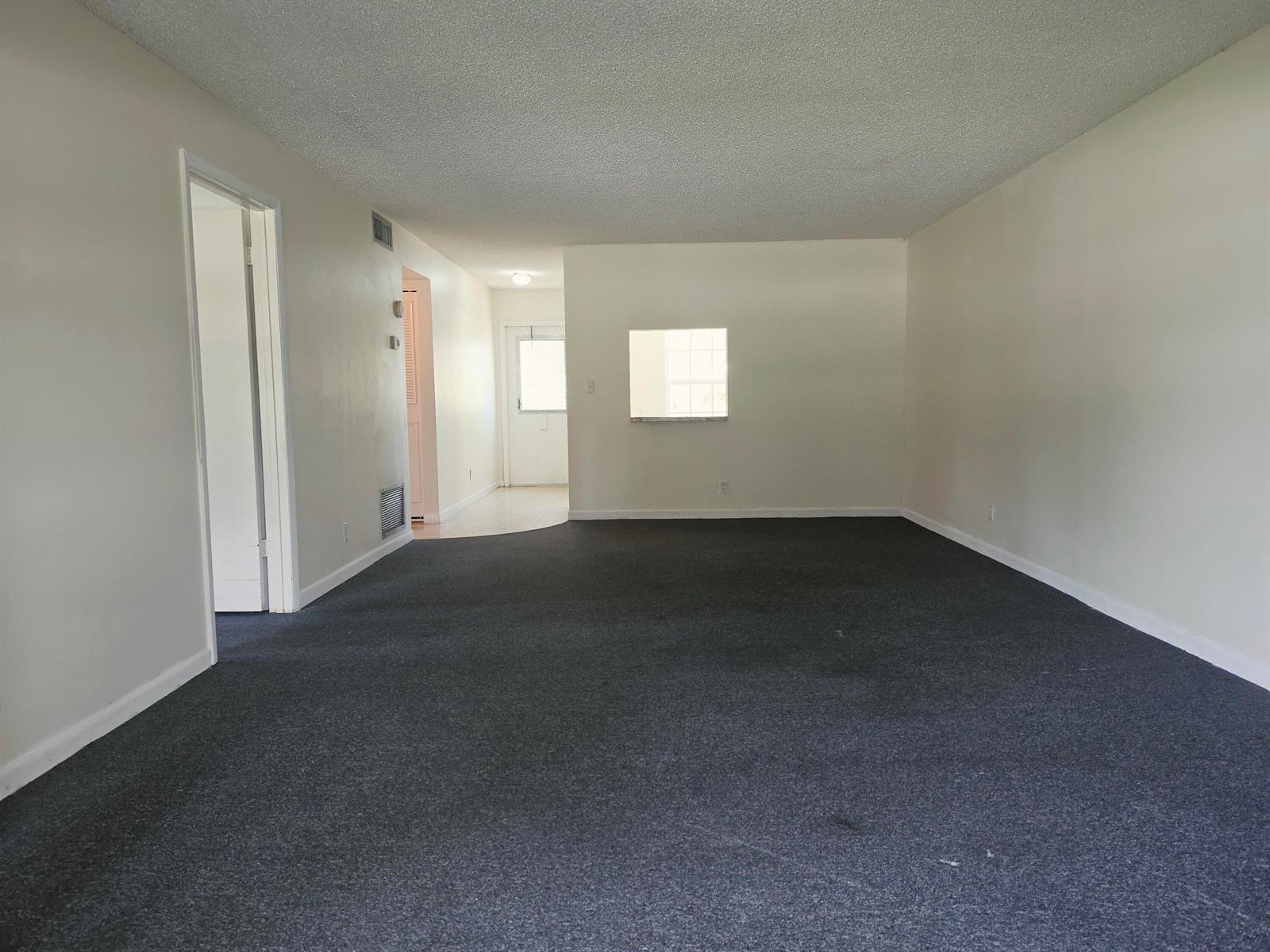 A living room with dark gray carpeting, white walls, and a small interior pass-through window — 713 Nantucket Circle # B, Lake Worth FL 33467, LAKE WORTH, FL