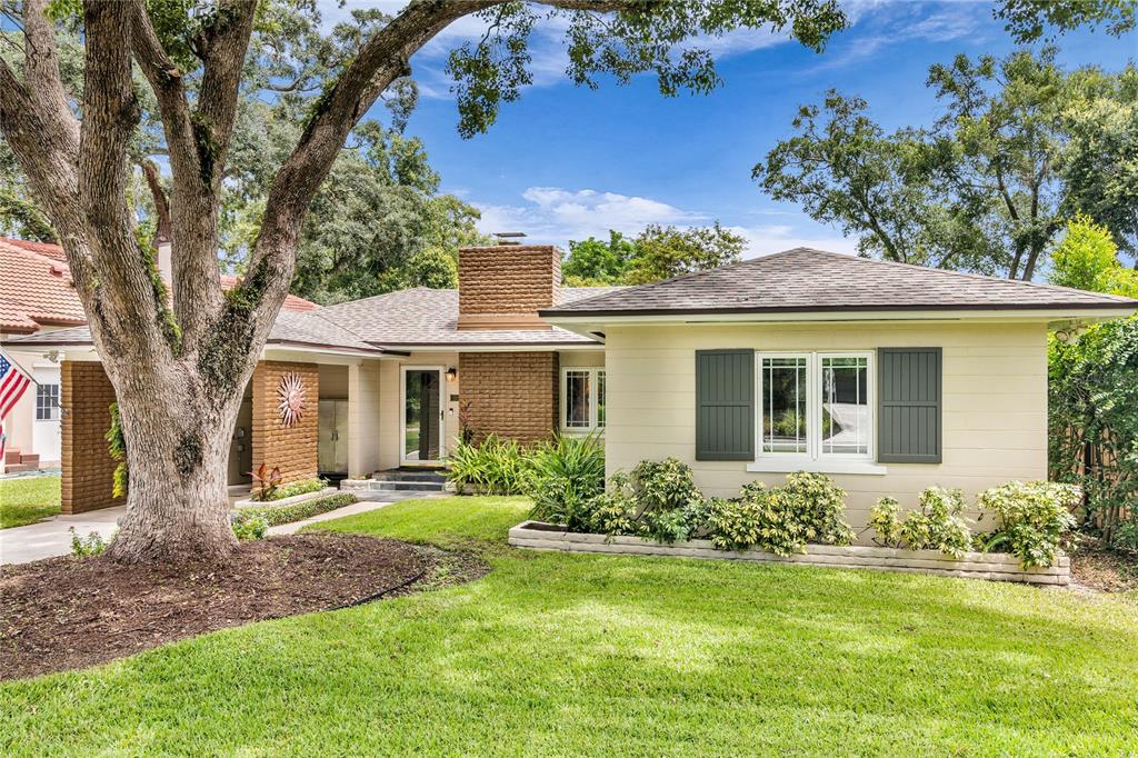 A single-story house with a brick chimney, tan siding, and a large tree in front — 1215 DELANEY PARK DRIVE, ORLANDO, FL