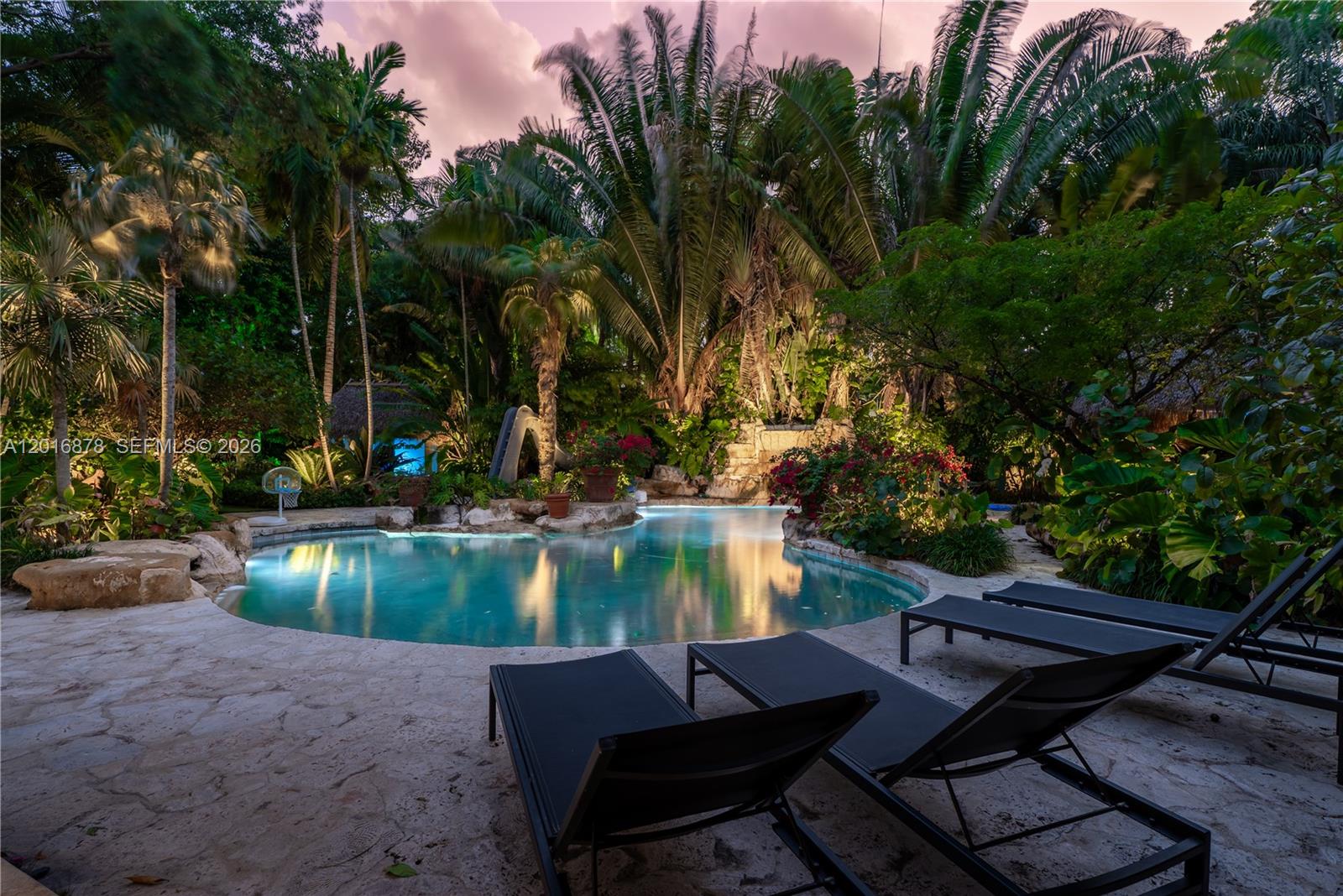 A tropical backyard features a curved swimming pool with a rock waterfall and lounge chairs — 8550 Old Cutler Rd, Coral Gables FL 33143, CORAL GABLES, FL