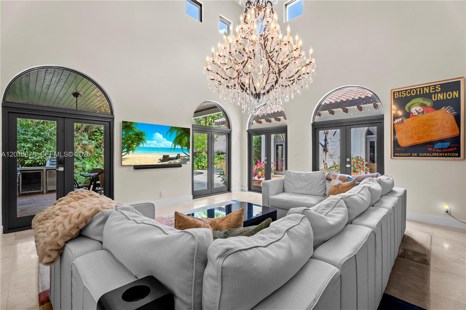 A high-ceilinged living room features a large crystal chandelier, a sectional sofa, and arched doors — 8550 Old Cutler Rd, Coral Gables FL 33143, CORAL GABLES, FL