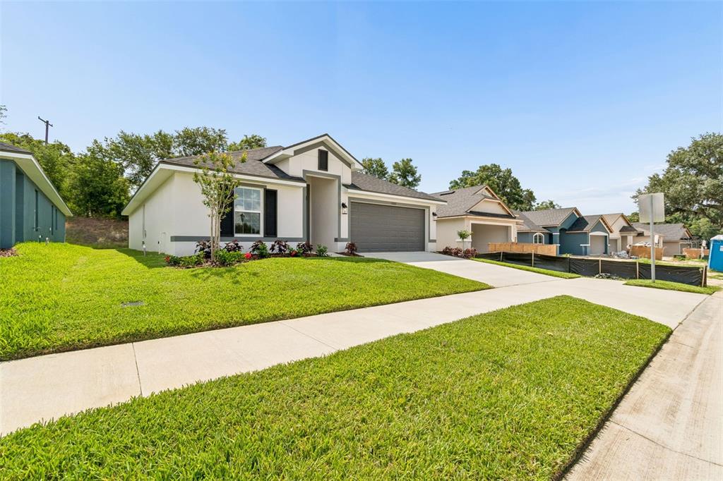 A single-story suburban house with a gray garage and white stucco exterior under a blue sky — 13000 KENT BRADLEY STREET, DADE CITY, FL