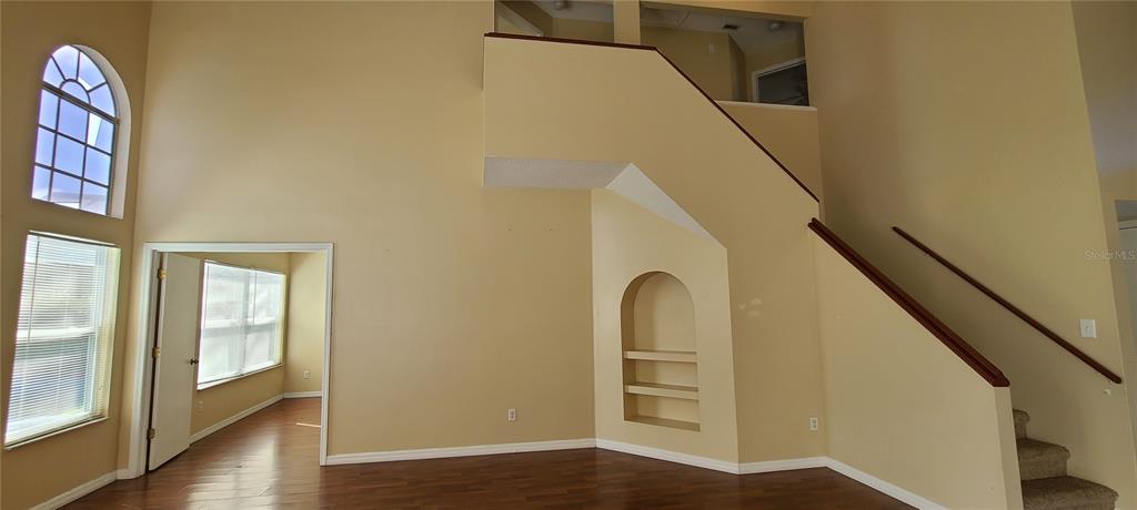 A living room with high ceilings, a staircase, a built-in niche, and wood flooring — 2411 BERKSHIRE COURT, KISSIMMEE, FL
