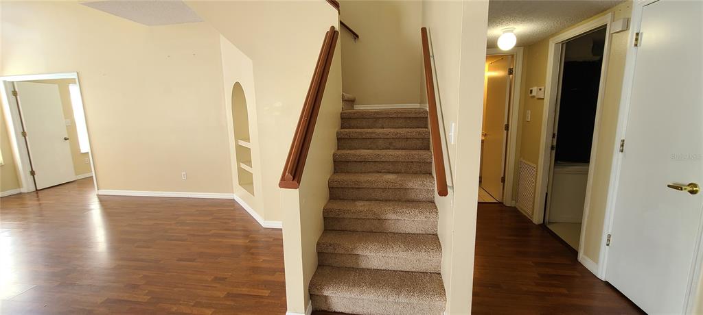 A carpeted staircase sits between a wood-floored living area and a hallway with white doors — 2411 BERKSHIRE COURT, KISSIMMEE, FL