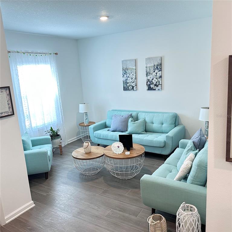 A living room features light blue sofas, two round coffee tables, and wood-look tile flooring — 6459 PINE FORK ALLEY, ST CLOUD, FL