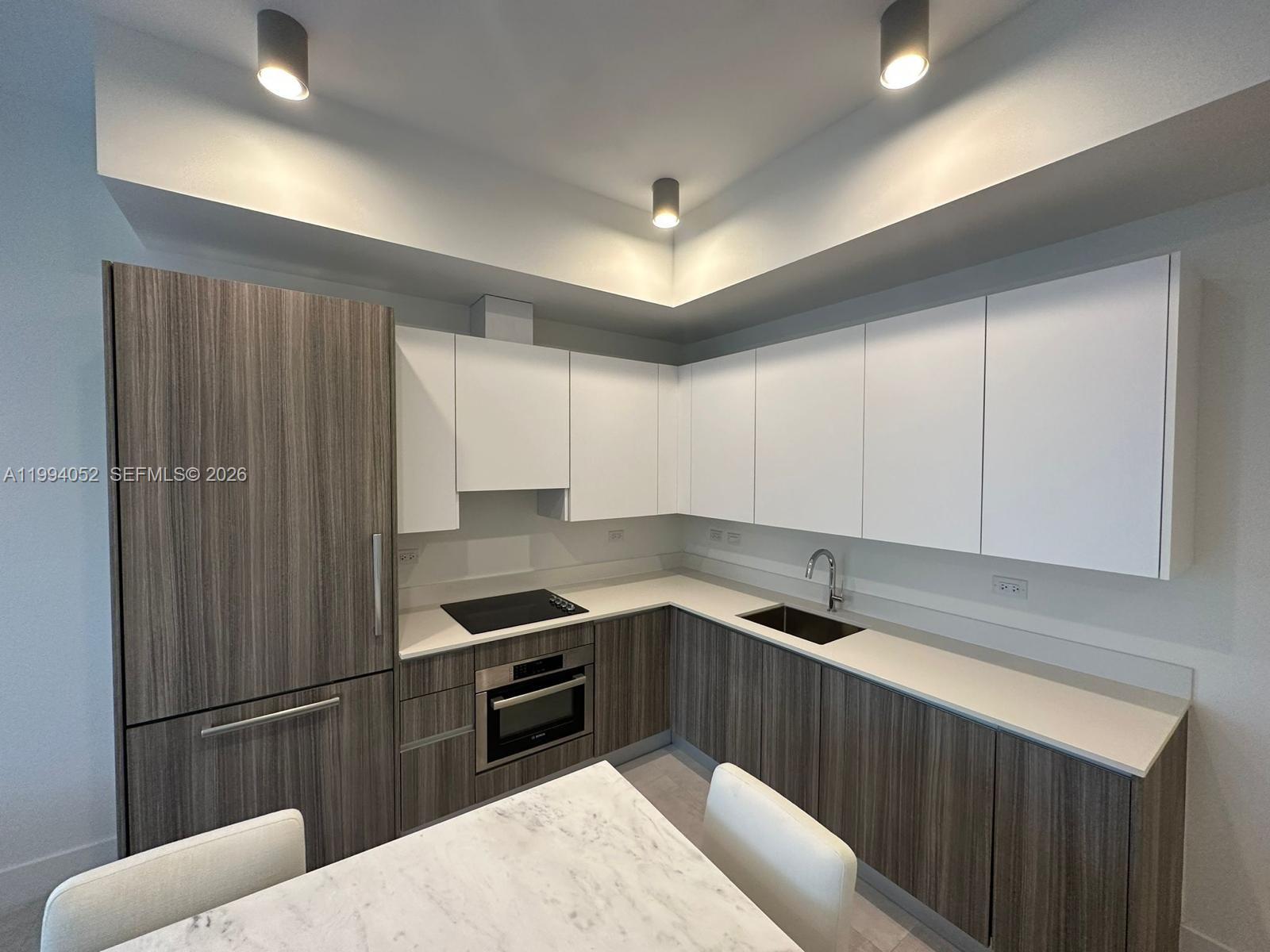 A modern kitchen features wood-grain cabinetry, white upper cabinets, and white countertops — 239 SW 9th St # 2002, Miami FL 33130, MIAMI, FL