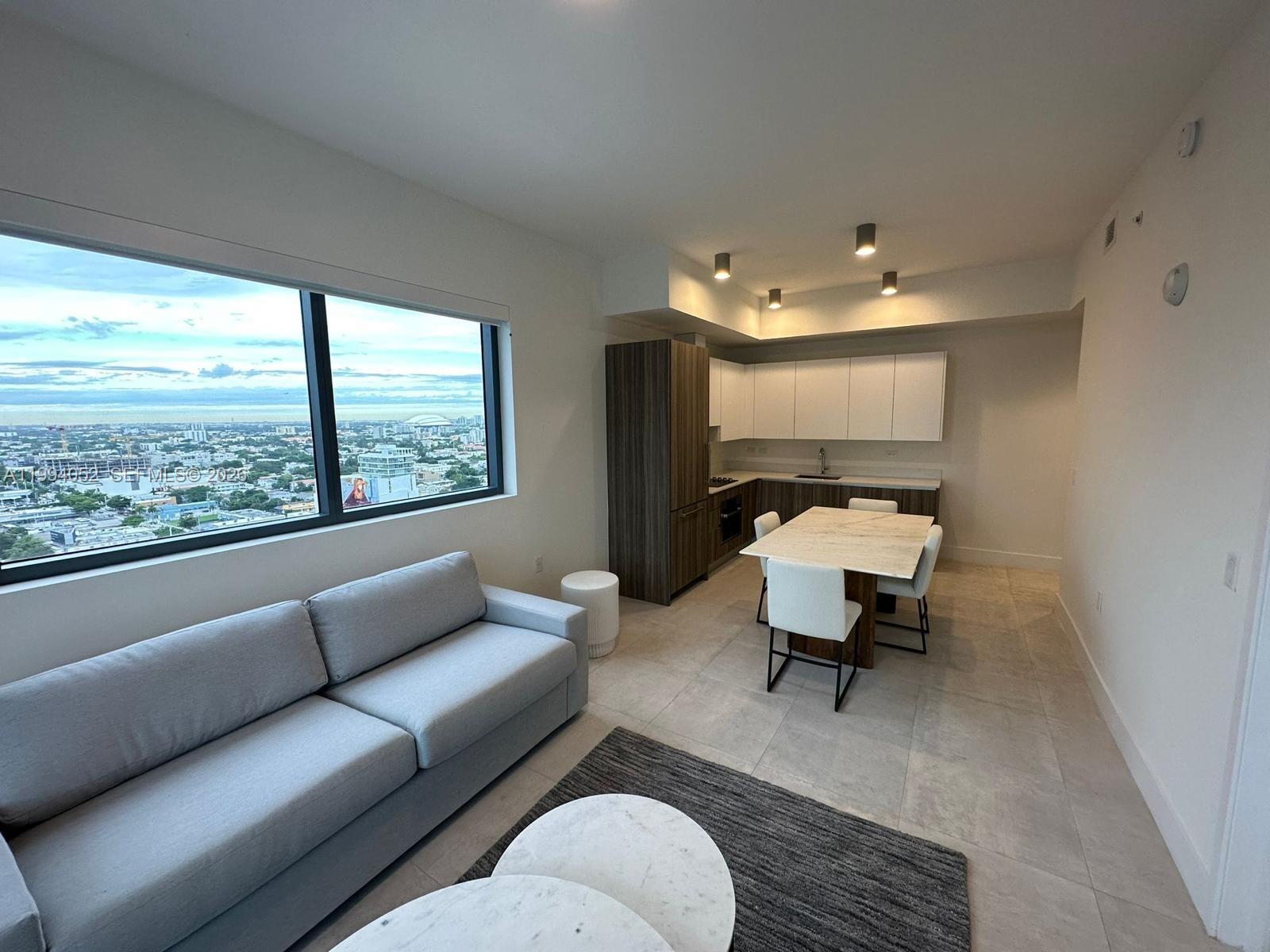 A modern apartment living area features a grey sofa, dining table, and floor-to-ceiling windows — 239 SW 9th St # 2002, Miami FL 33130, MIAMI, FL
