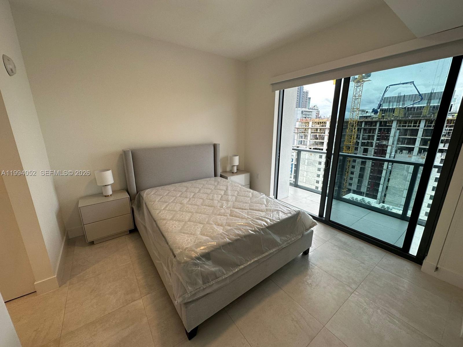 A bedroom with a bed, two nightstands, and a balcony overlooking a construction site — 239 SW 9th St # 2002, Miami FL 33130, MIAMI, FL