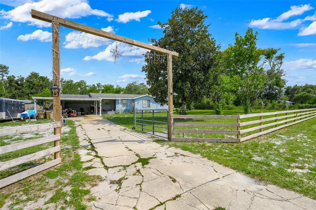A cracked concrete driveway leads to a single-story house behind a wooden gate and fence — 26106 FISHERMANS ROAD, PAISLEY, FL