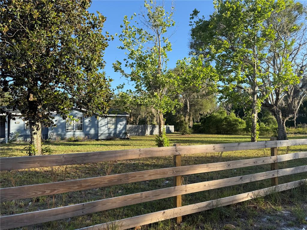 A wooden fence borders a grassy yard with trees and a light blue house — 26106 FISHERMANS ROAD, PAISLEY, FL