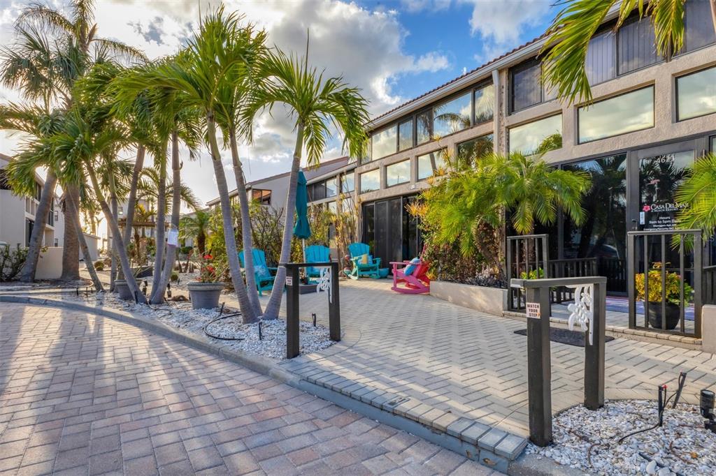 A paved courtyard features palm trees, colorful Adirondack chairs, and a multi-story building exterior — 4621 GULF OF MEXICO DRIVE UNIT 10D, LONGBOAT KEY, FL