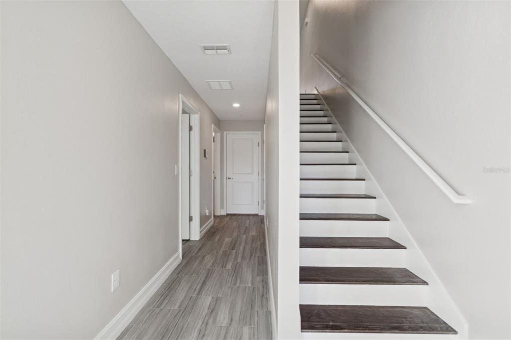 A hallway with wood-look tile flooring leads to a closed door beside a staircase — 4921 W PAUL AVENUE UNIT 4, TAMPA, FL