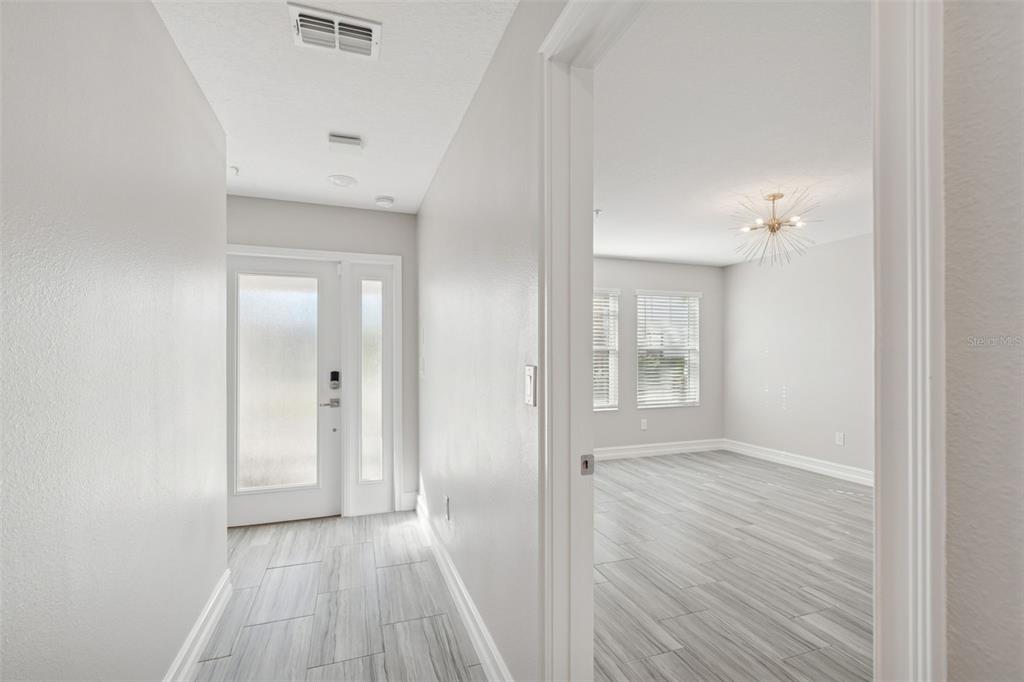 A bright entryway with light-colored wood-look tile flooring leads into a room with a chandelier — 4921 W PAUL AVENUE UNIT 4, TAMPA, FL