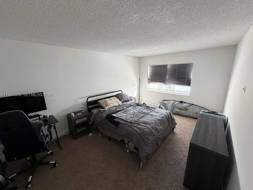 A bedroom features a bed, a desk with a chair, and a dresser on carpet — 488 NW 165th St Rd # 614, Miami FL 33169, MIAMI, FL