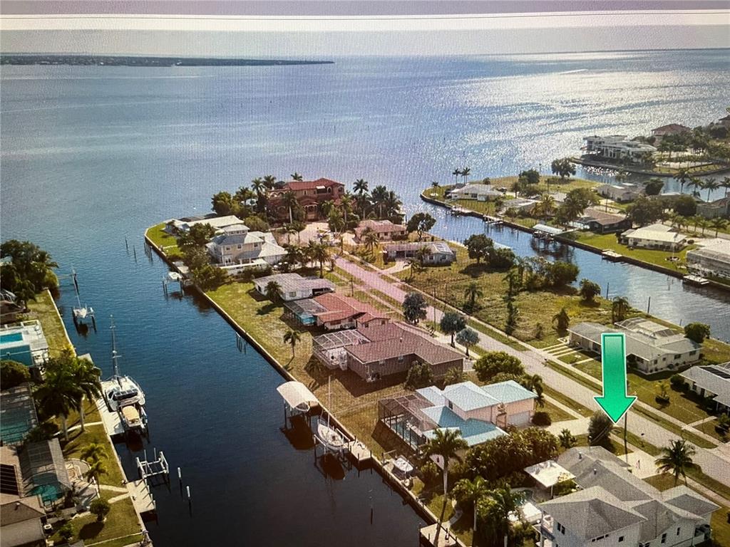 An aerial view shows a waterfront residential neighborhood with a green arrow pointing to a house — 217 BANGSBERG ROAD SE, PORT CHARLOTTE, FL