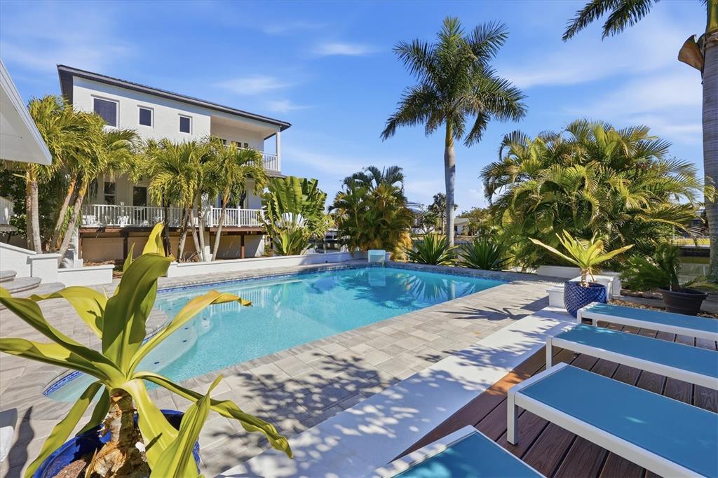 A swimming pool sits on a stone patio next to a house with palm trees — 217 BANGSBERG ROAD SE, PORT CHARLOTTE, FL
