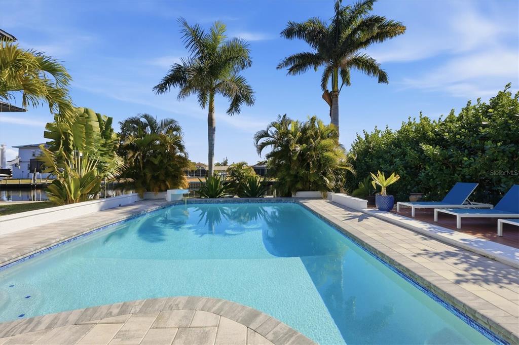 A swimming pool with a stone deck is surrounded by palm trees and lush landscaping — 217 BANGSBERG ROAD SE, PORT CHARLOTTE, FL