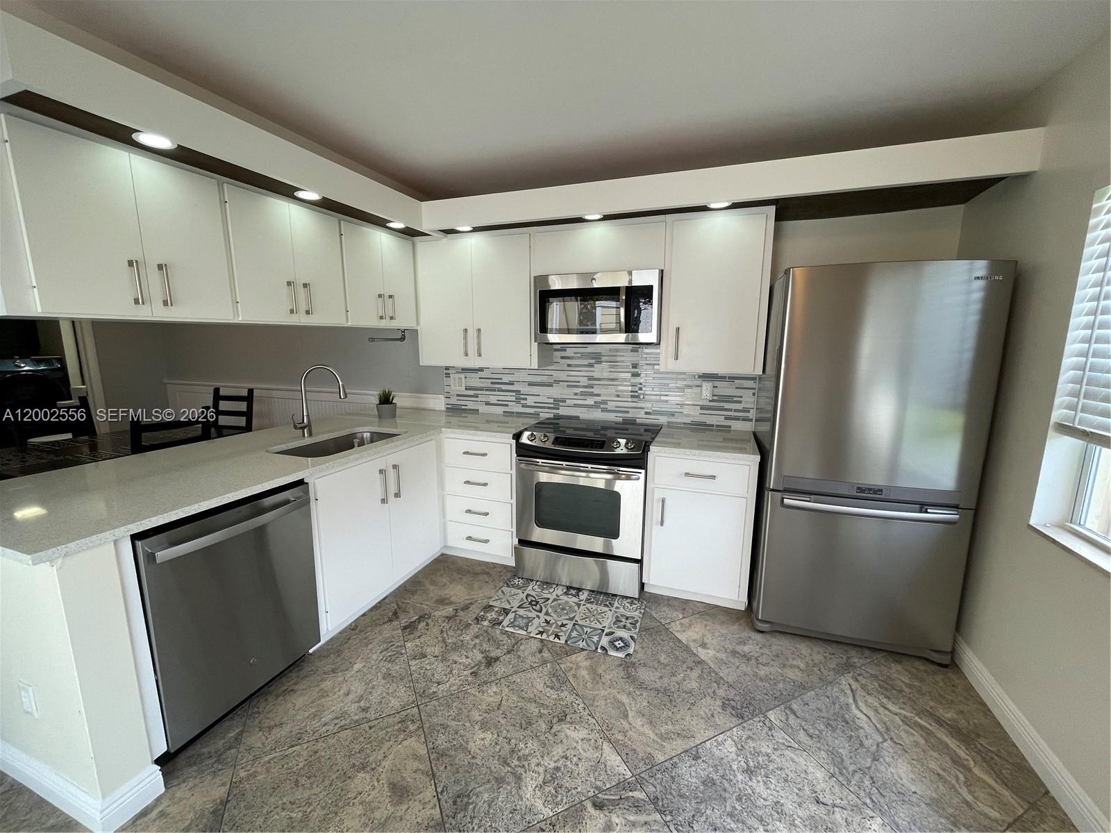 A kitchen with stainless steel appliances, gray tile flooring, and a sliding glass door — 5801 Wheatley Ct, Boynton Beach FL 33436, BOYNTON BEACH, FL