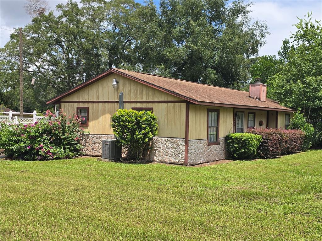 A single-story house with yellow vertical siding, stone veneer base, and a brown shingled roof — 5521 NE 4TH PLACE, OCALA, FL