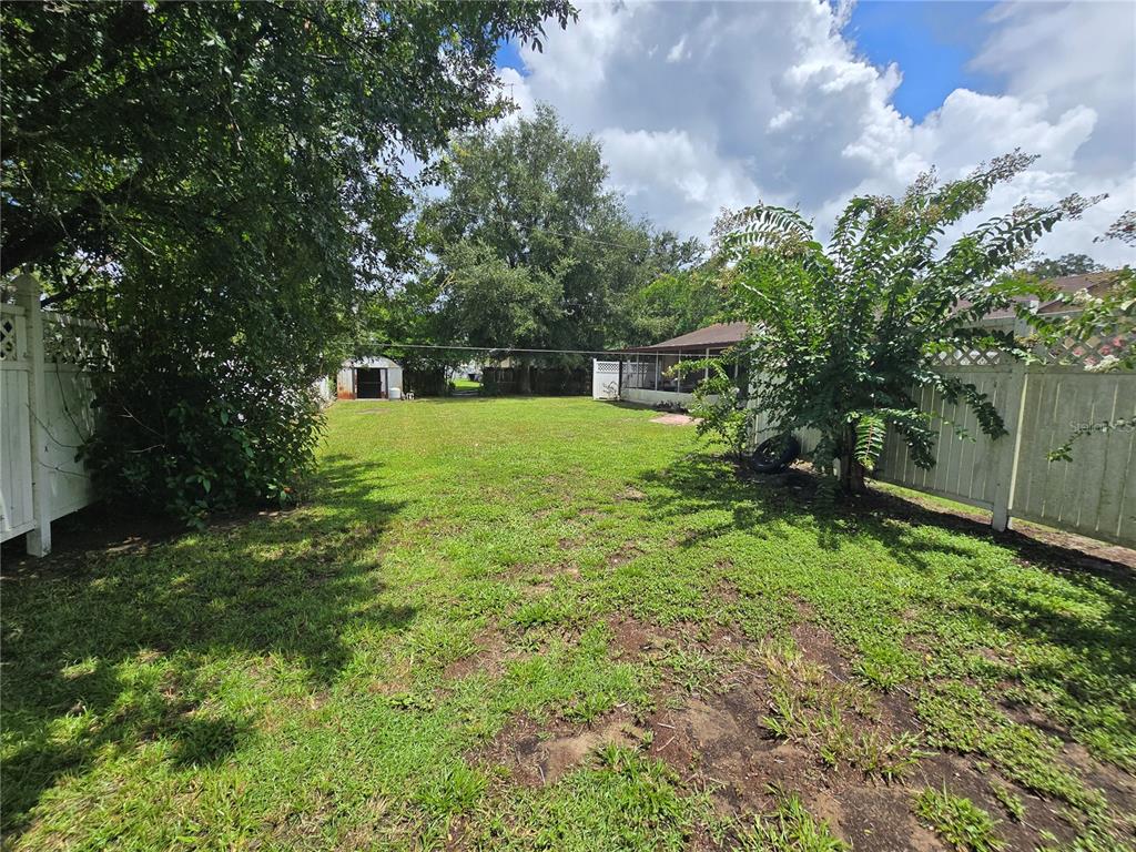 A grassy backyard features a white vinyl fence, a small shed, and a covered patio — 5521 NE 4TH PLACE, OCALA, FL