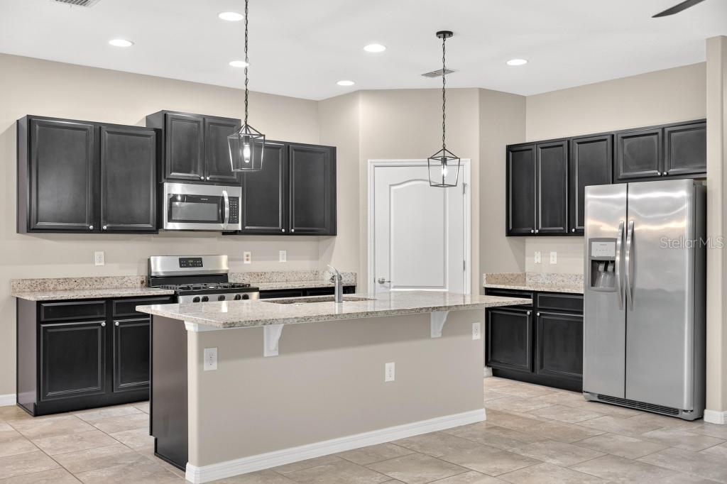 A kitchen with dark cabinets, granite countertops, stainless steel appliances, and a central island — 736 E VICTORIA TRAILS BOULEVARD, DELAND, FL