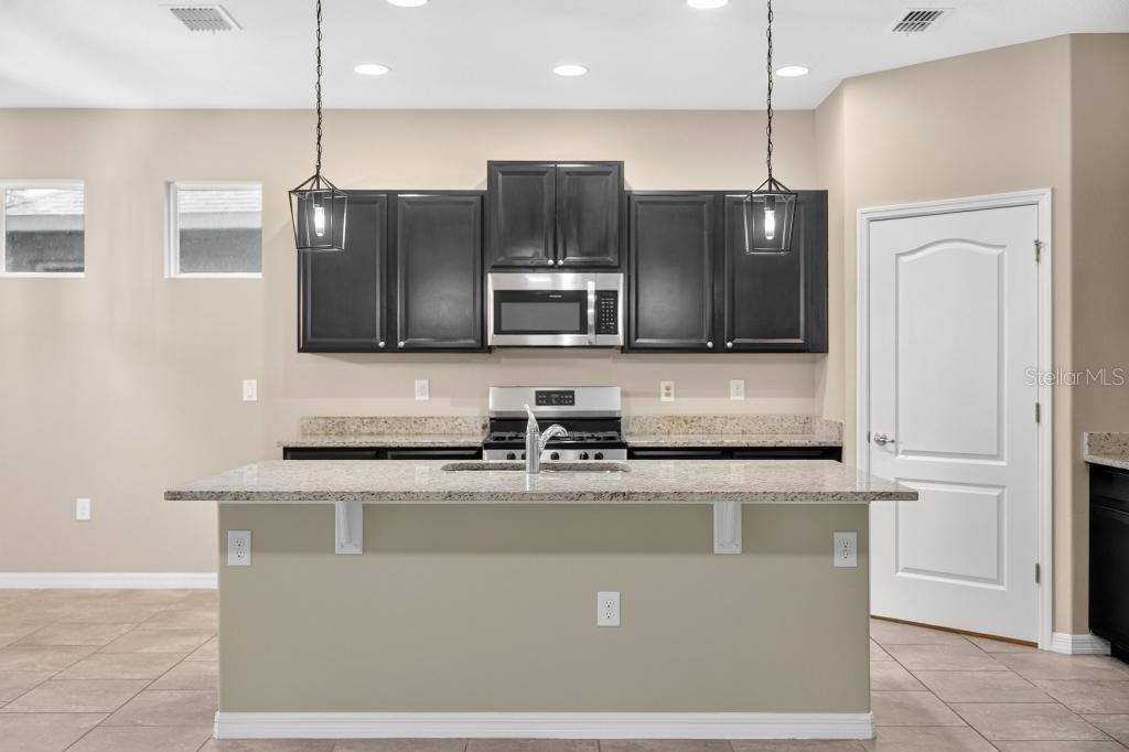 A kitchen features dark wood cabinets, granite countertops, a central island, and stainless steel appliances — 736 E VICTORIA TRAILS BOULEVARD, DELAND, FL