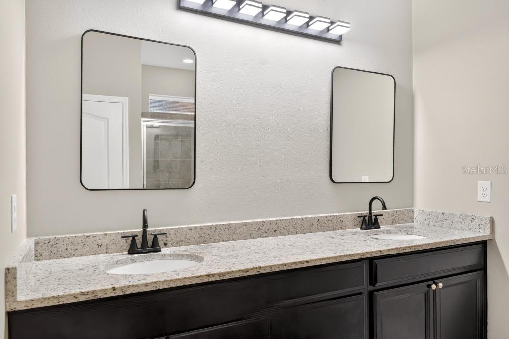 A bathroom vanity features a granite countertop, dual sinks, black cabinets, and two rectangular mirrors — 736 E VICTORIA TRAILS BOULEVARD, DELAND, FL