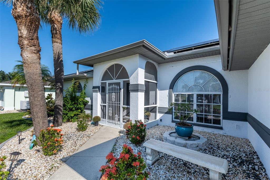 The exterior of a white house features a screened entryway, arched window, and palm trees — 538 W CASHEW, PUNTA GORDA, FL