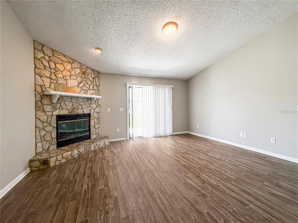 A living room features wood-look flooring, a stone corner fireplace, and sliding glass patio doors — 7966 AMANDAS CROSSING DRIVE E, JACKSONVILLE, FL
