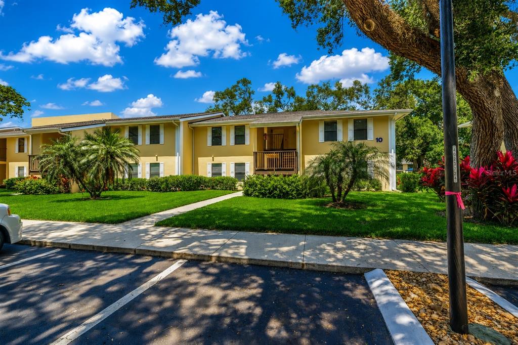 A two-story yellow apartment building with a sidewalk and palm trees in the foreground — 3001 58TH AVENUE S UNIT 1014, ST PETERSBURG, FL