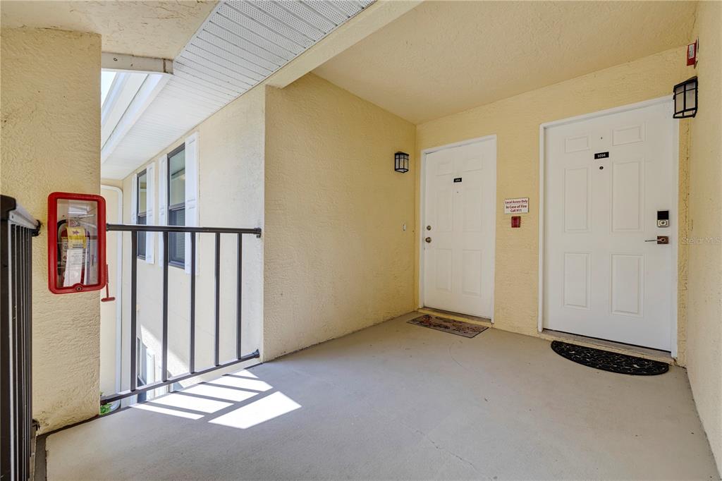 An outdoor apartment hallway with two white doors, a fire extinguisher, and a metal railing — 3001 58TH AVENUE S UNIT 1014, ST PETERSBURG, FL