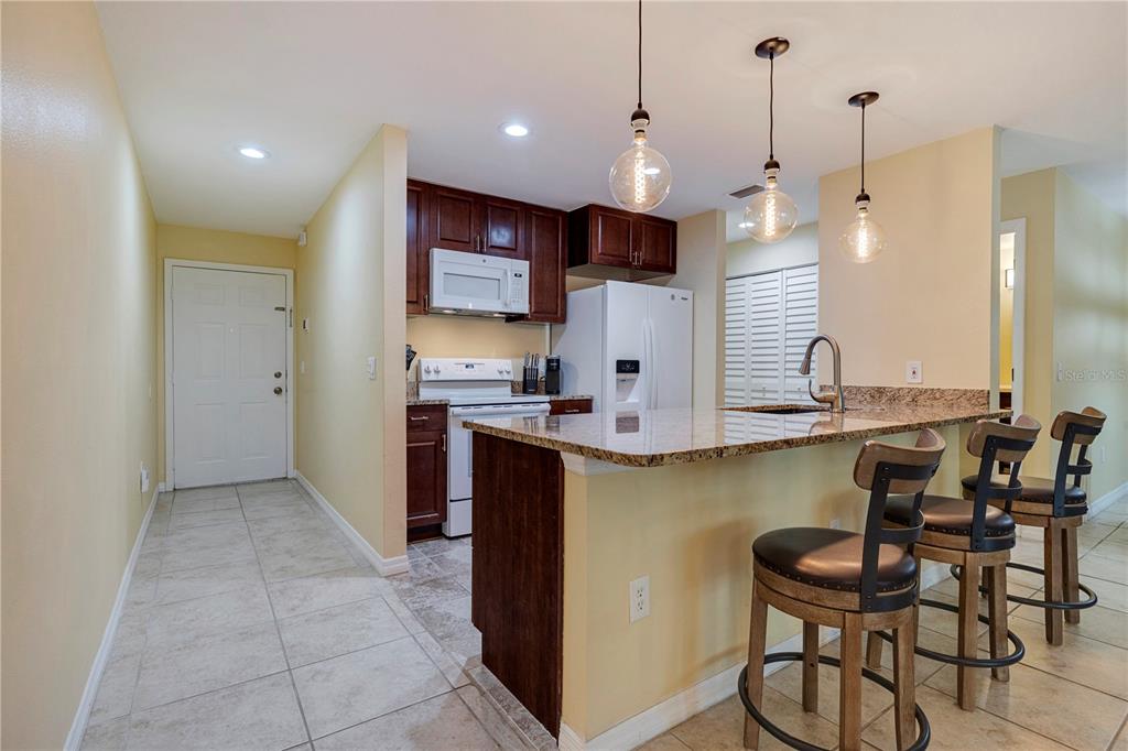 A kitchen features dark wood cabinets, granite countertops, a breakfast bar, and three pendant lights — 3001 58TH AVENUE S UNIT 1014, ST PETERSBURG, FL