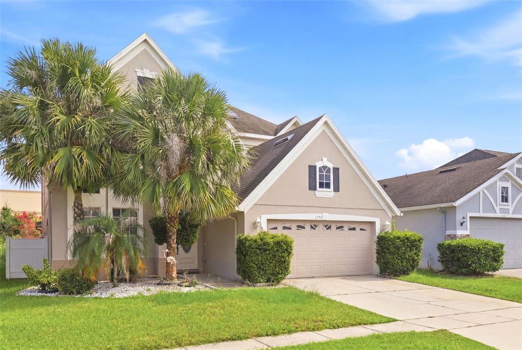 A two-story suburban house with a tan stucco exterior, a two-car garage, and palm trees — 1357 DARNABY WAY, ORLANDO, FL