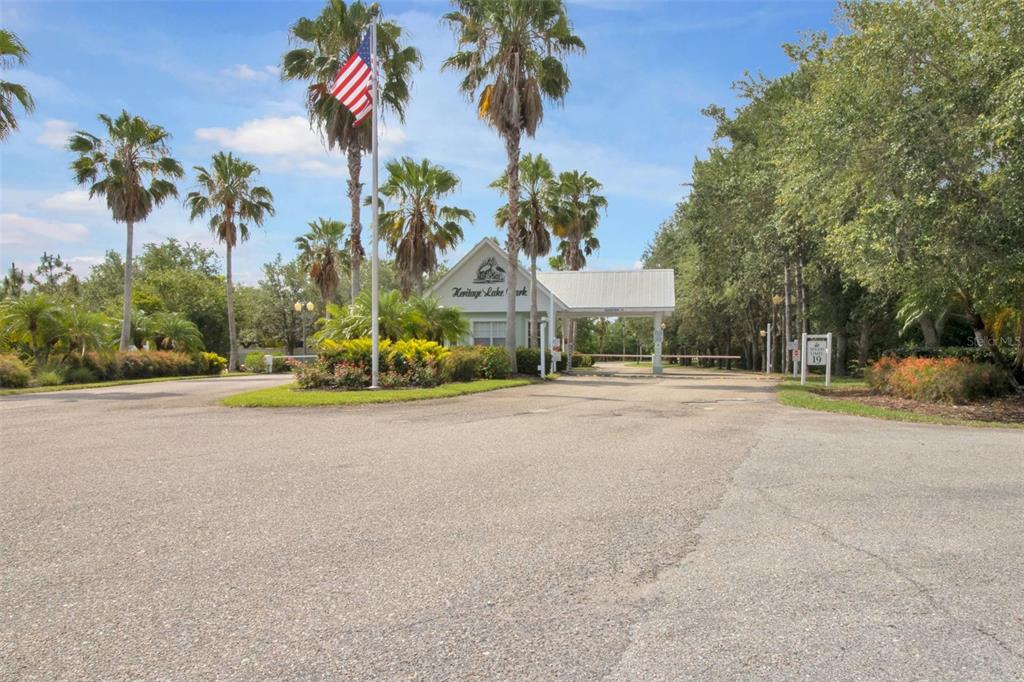 The gated entrance to Heritage Lake Park features a guardhouse, palm trees, and an American flag — 2140 HERON LAKE DRIVE UNIT 204, PUNTA GORDA, FL