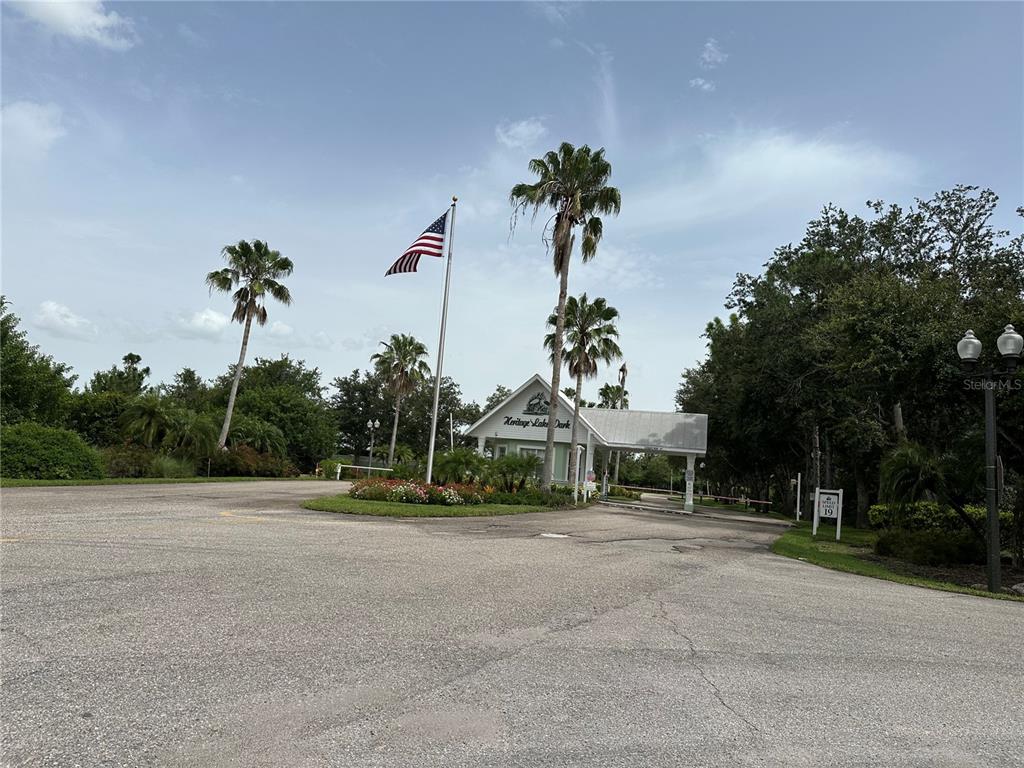 An entrance gate with a flag and palm trees leads into Heritage Lake Park — 2140 HERON LAKE DRIVE UNIT 204, PUNTA GORDA, FL