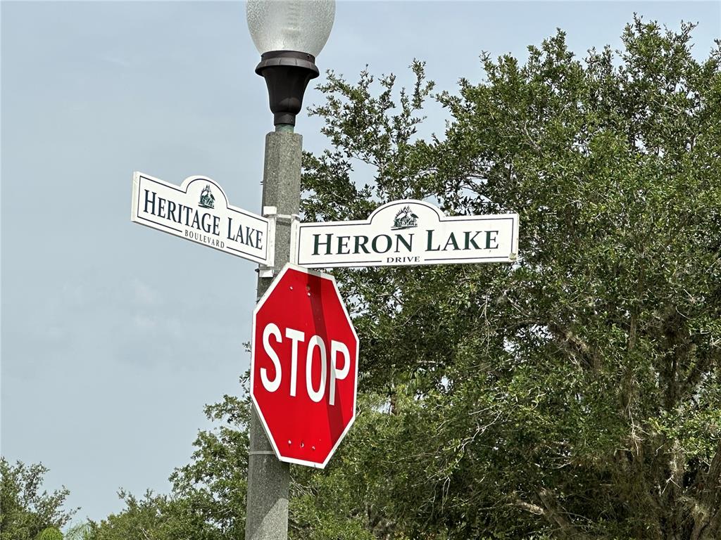 A stop sign is mounted on a pole below two street signs for Heritage Lake Boulevard — 2140 HERON LAKE DRIVE UNIT 204, PUNTA GORDA, FL