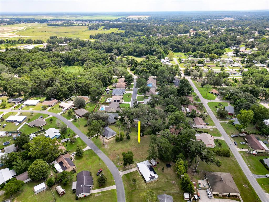 An aerial view shows a vacant residential lot marked by a yellow arrow — TBD SE 54TH AVENUE, BELLEVIEW, FL