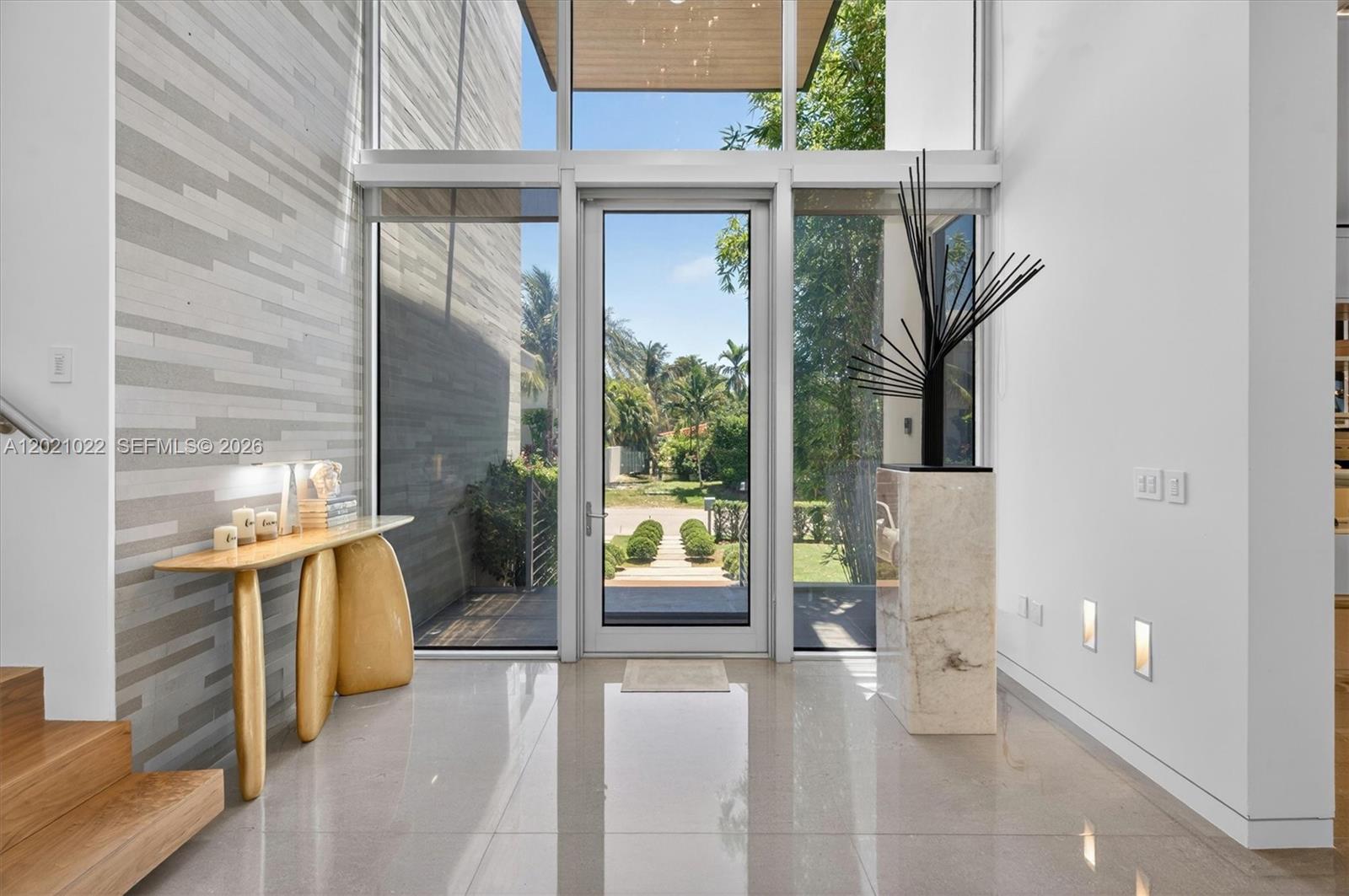 A modern entryway features a glass front door, stone tile floors, and a sculptural accent piece — 625 Curtiswood Dr, Key Biscayne FL 33149, KEY BISCAYNE, FL