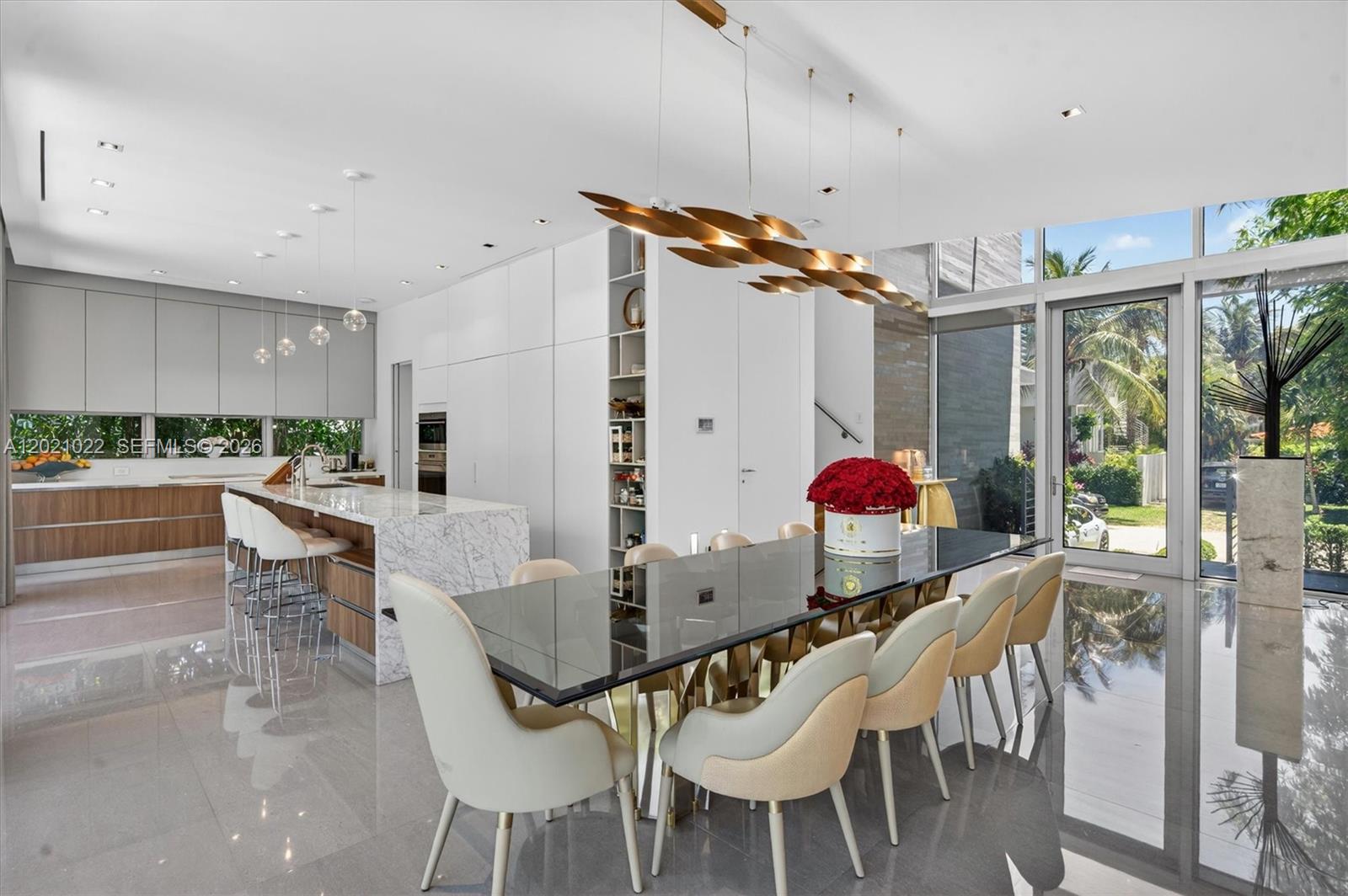 A modern dining area and kitchen feature a marble island, glass table, and floor-to-ceiling windows — 625 Curtiswood Dr, Key Biscayne FL 33149, KEY BISCAYNE, FL