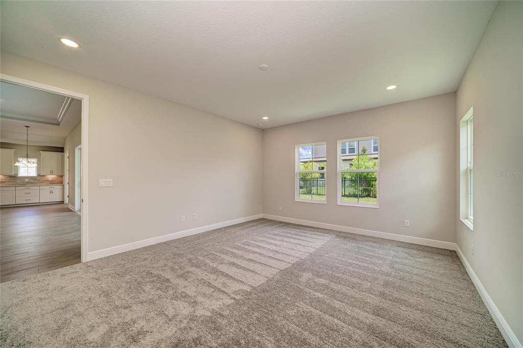 An empty room with gray carpet, neutral walls, recessed lighting, and windows overlooking a yard — 5237 WOLF CREEK DRIVE, APOLLO BEACH, FL