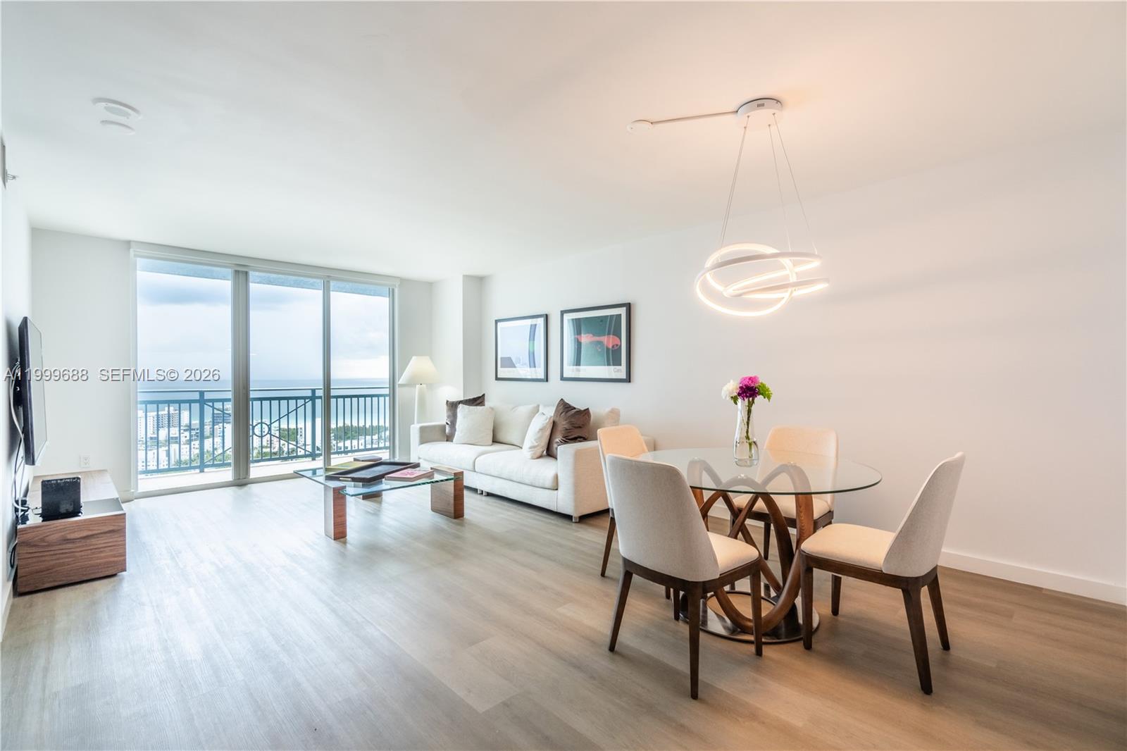 A bright living and dining area features light wood floors, a glass table, and balcony views — 90 Alton Rd # 2807, Miami Beach FL 33139, MIAMI BEACH, FL