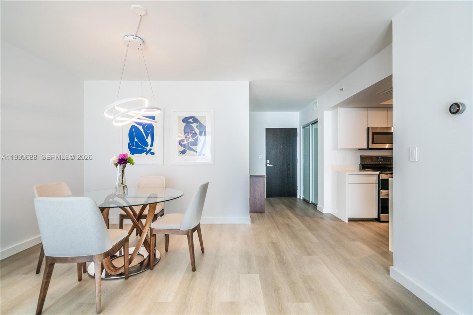 A dining area with a glass table and modern light fixture sits near a kitchen — 90 Alton Rd # 2807, Miami Beach FL 33139, MIAMI BEACH, FL