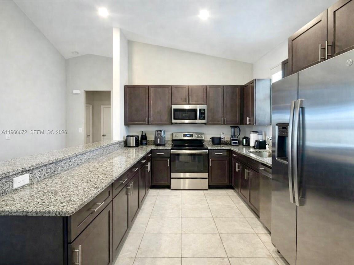 A kitchen features dark wood cabinets, granite countertops, and stainless steel appliances — 9042 E Broad Circle, La Belle FL 33935, LA BELLE, FL