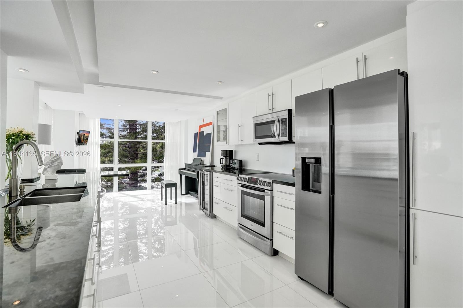 A modern white kitchen features stainless steel appliances, glossy tile floors, and floor-to-ceiling windows — 1000 Parkview Dr # 330, Hallandale Beach FL 33009, HALLANDALE BEACH, FL
