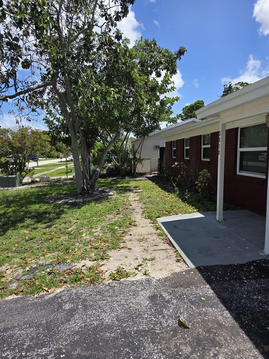 A brick house exterior features a concrete walkway, a large tree, and a paved driveway — 3818 Everglades Road, FL 33410, FL