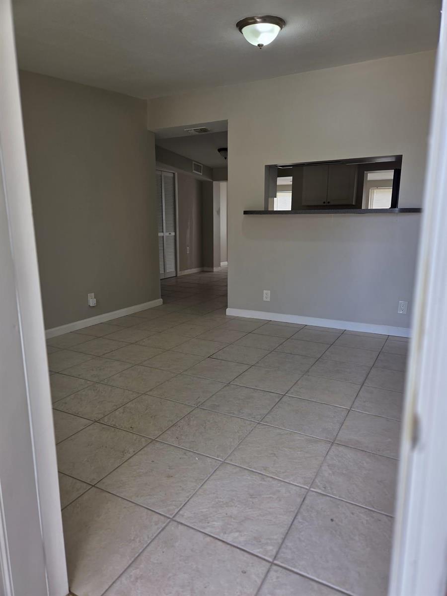 An empty room with beige tile flooring, gray walls, and a kitchen pass-through window — 3818 Everglades Road, FL 33410, FL