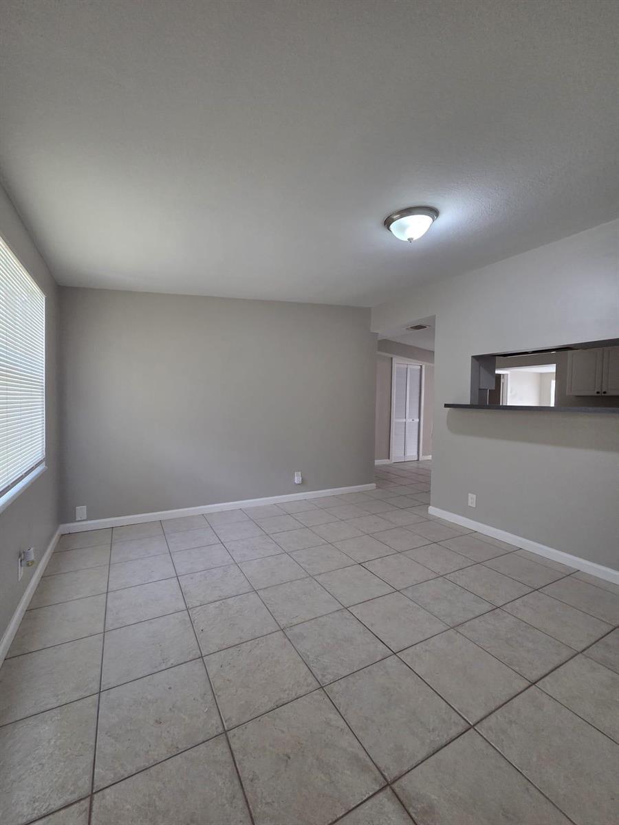 An empty room with light gray walls, tile flooring, and a kitchen pass-through window — 3818 Everglades Road, FL 33410, FL