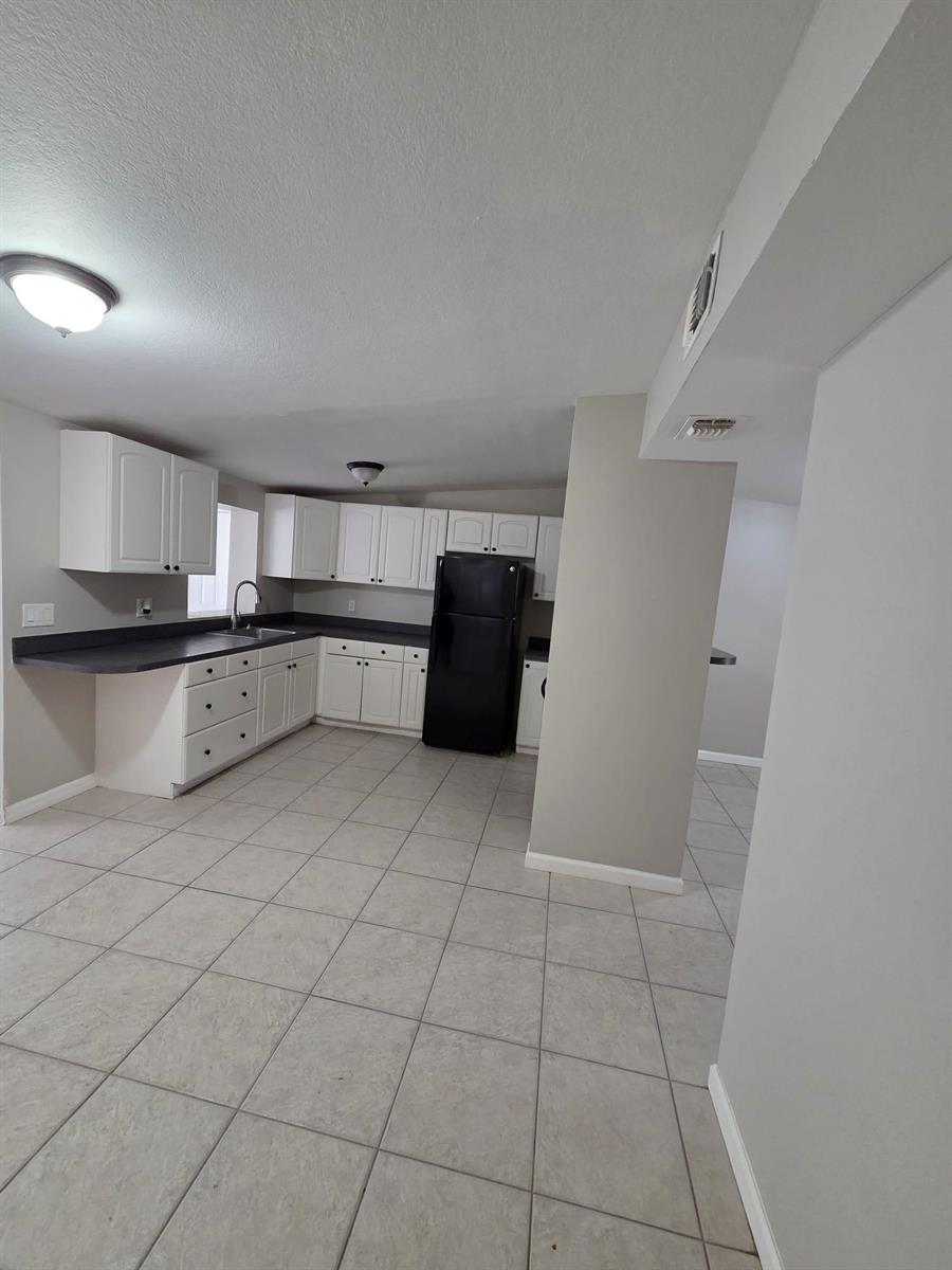 A kitchen with white cabinets, dark countertops, a black refrigerator, and light-colored tile flooring — 3818 Everglades Road, FL 33410, FL