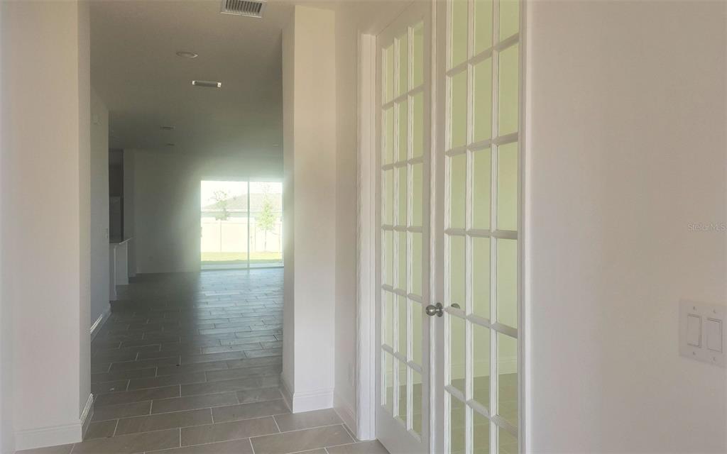 A hallway with tile flooring leads to a bright living area with glass sliding doors — 14574 CRESTAVISTA AVENUE, CLERMONT, FL