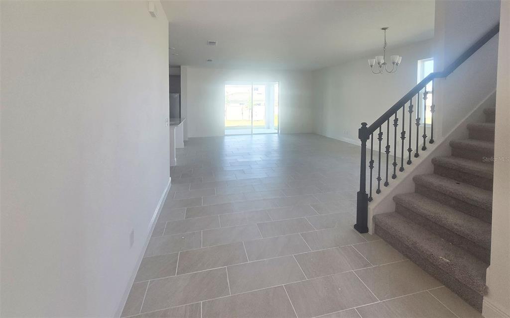 An open-concept living area features light gray tile flooring, a staircase, and sliding glass doors — 14574 CRESTAVISTA AVENUE, CLERMONT, FL